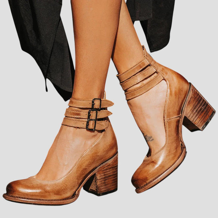 A woman wearing cognac block-heel pumps with triple ankle straps and a rounded toe.
