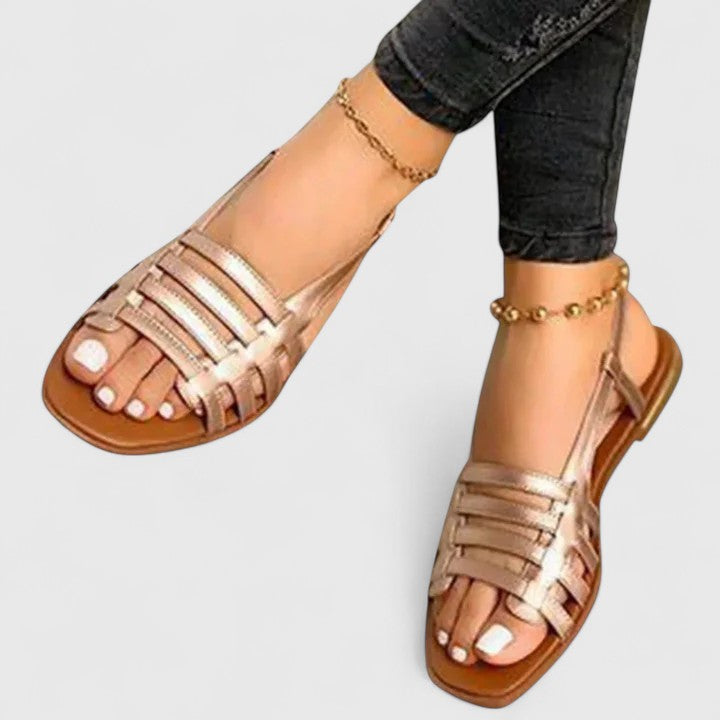 A woman wearing gold refined comfort sandals with a broad, cushioned footbed.