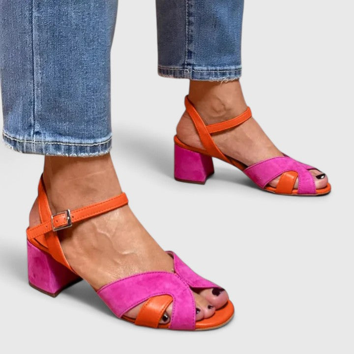 A woman wearing pink and orange open-toe block-heel sandals with an ankle strap, standing comfortably in a summer outfit.