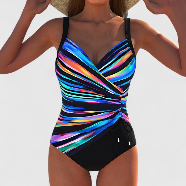A woman by the water in an elegant printed swimsuit, poised and confident in the summer sun.