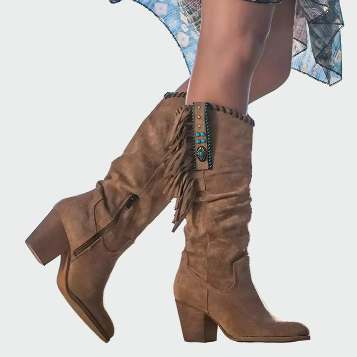 Woman wearing tan fringed boho-Western knee-high boots with a floaty dress at a festival.