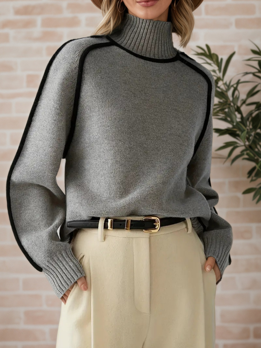 A woman wearing a funnel neck sweater with contrast piping, styled with pants for a smart-casual look.
