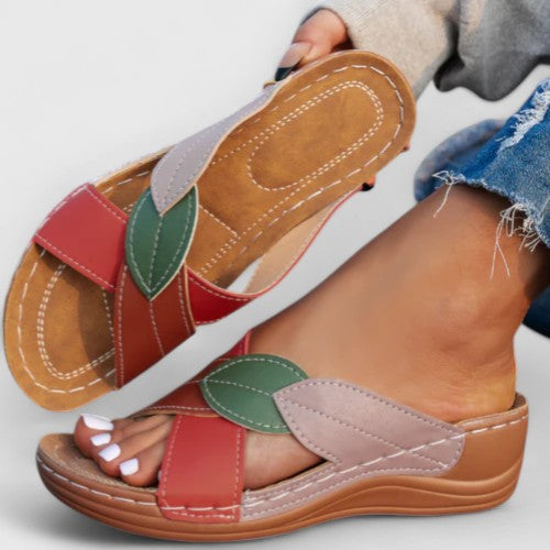 A woman wearing colourful leaf-print sandals with a cushioned insole and easy slip-on design.