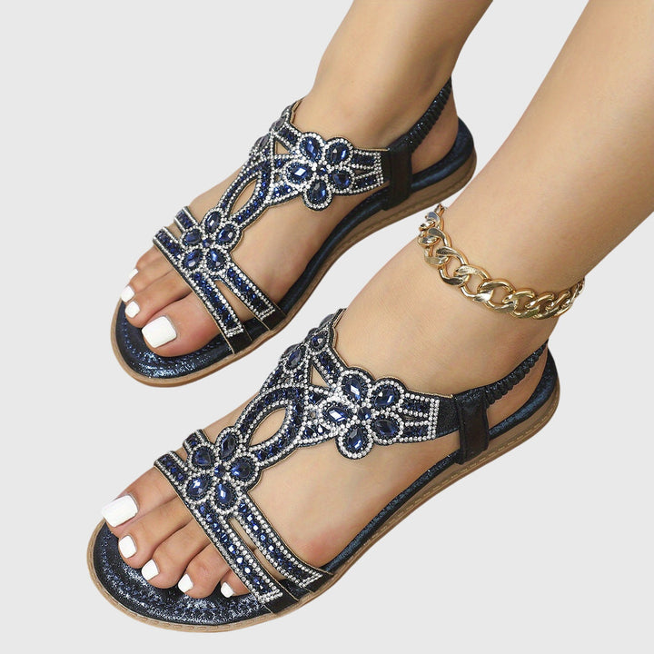 A woman wearing sky blue jewelled sandals with sparkling stones across the straps and a stretchy slingback.