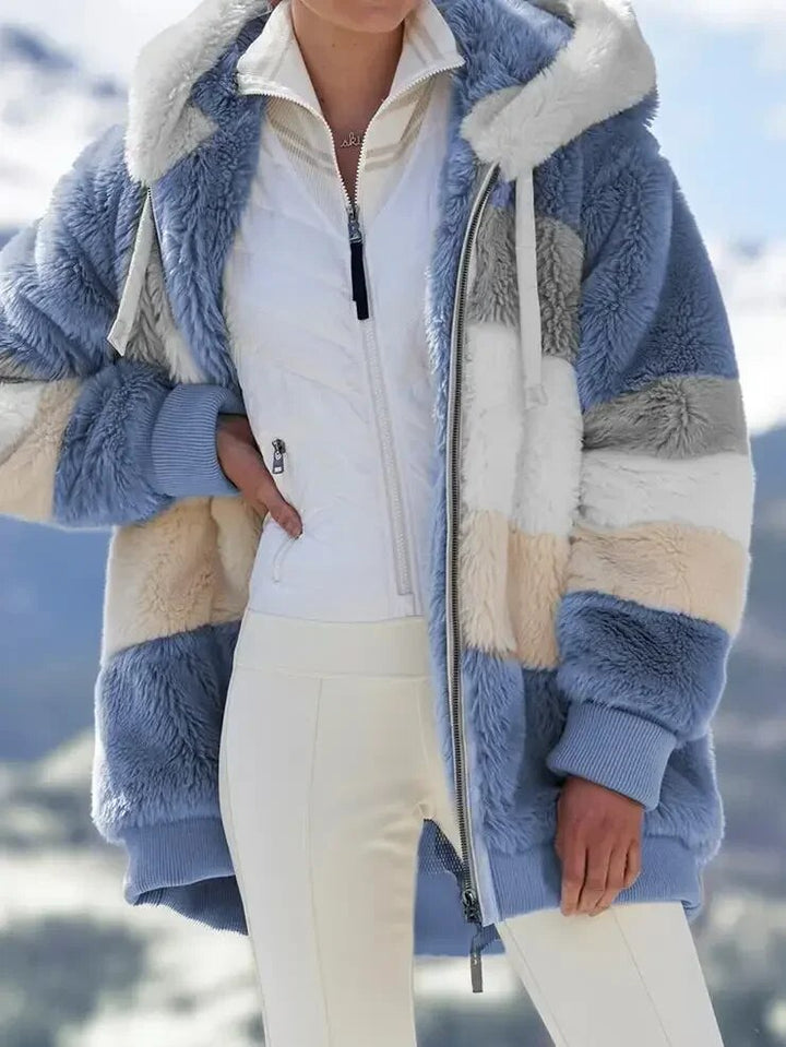 A woman wearing a plush oversized hooded zip jacket in blue and cream colour-block panels.