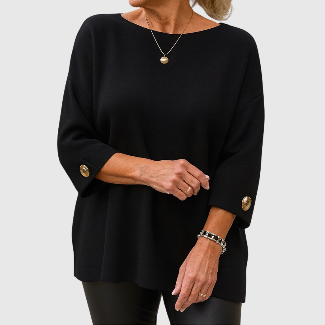 A woman wearing a cream sweater with a wide round neck and gold-toned buttons on the cuffs.