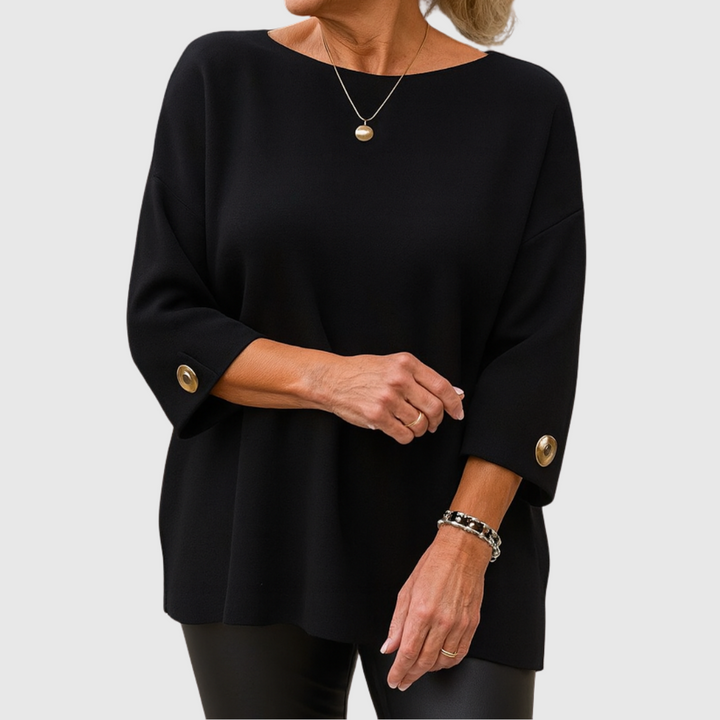 A woman wearing a cream sweater with a wide round neck and gold-toned buttons on the cuffs.