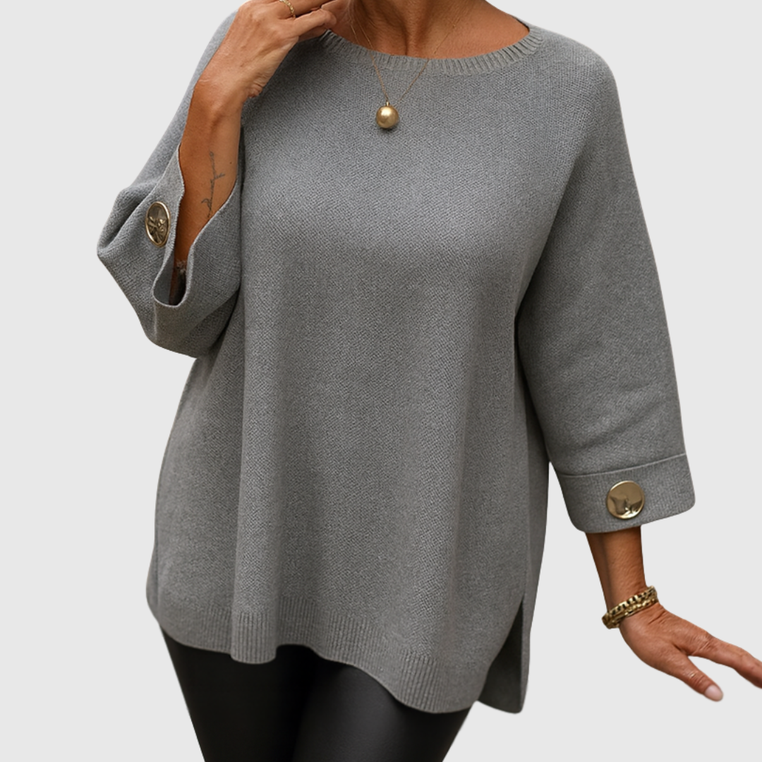 A woman wearing a cream sweater with a wide round neck and gold-toned buttons on the cuffs.