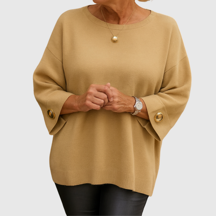 A woman wearing a cream sweater with a wide round neck and gold-toned buttons on the cuffs.