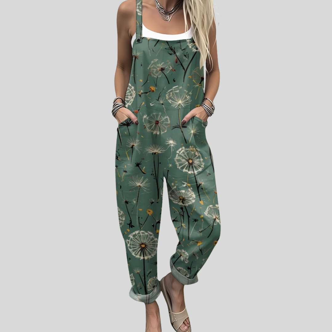 Woman wearing sage green overalls printed with delicate dandelion seed-heads, standing in gentle sunlight.