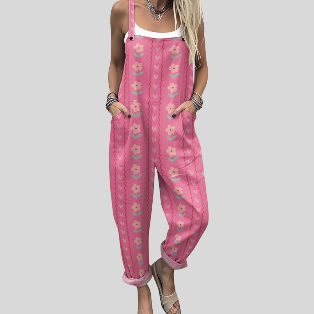 A woman wearing warm pink overalls printed with small flowers and hearts, smiling on a bright day.