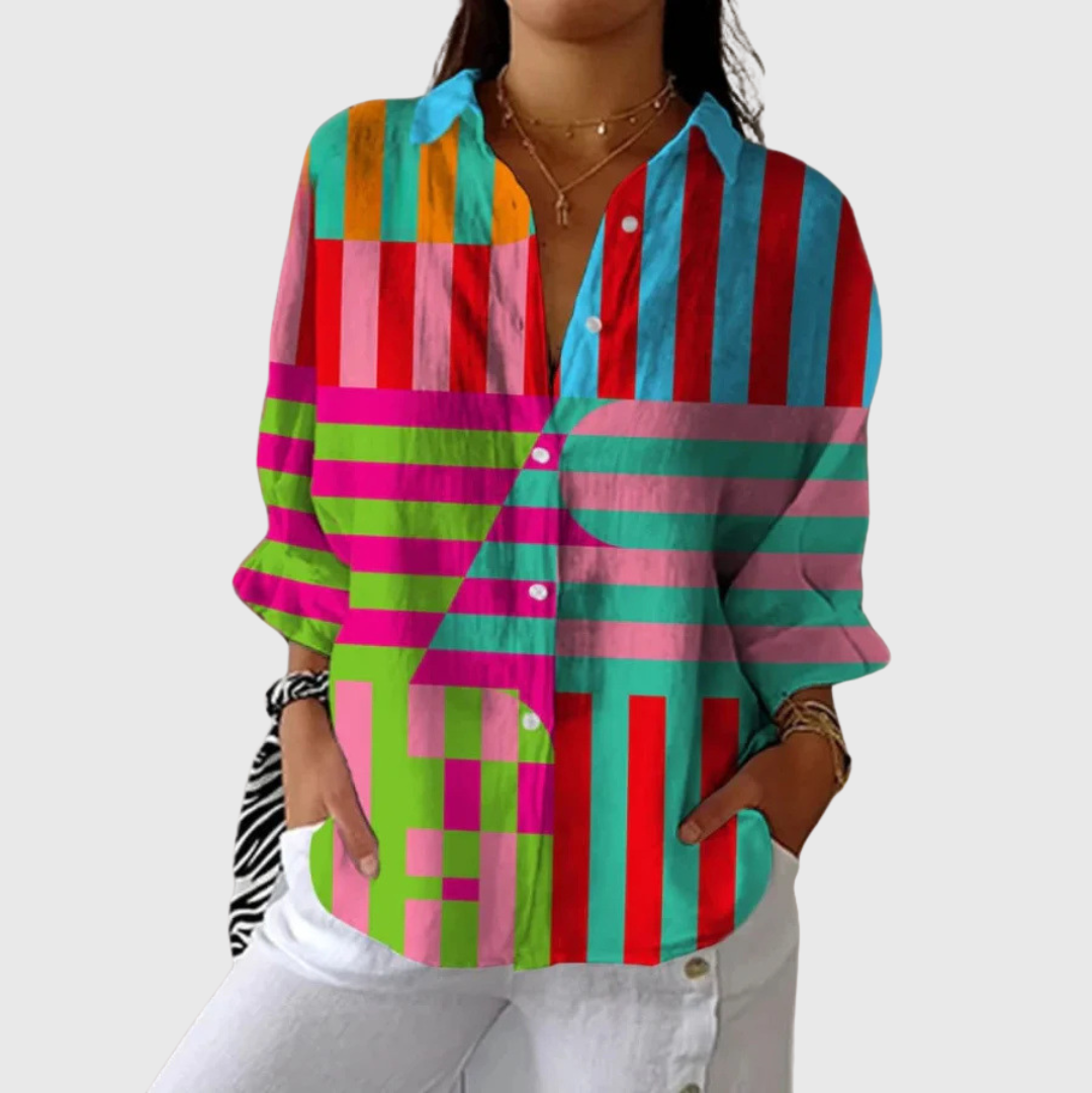 A woman wearing a bold multicoloured striped blouse, relaxed and smiling outdoors