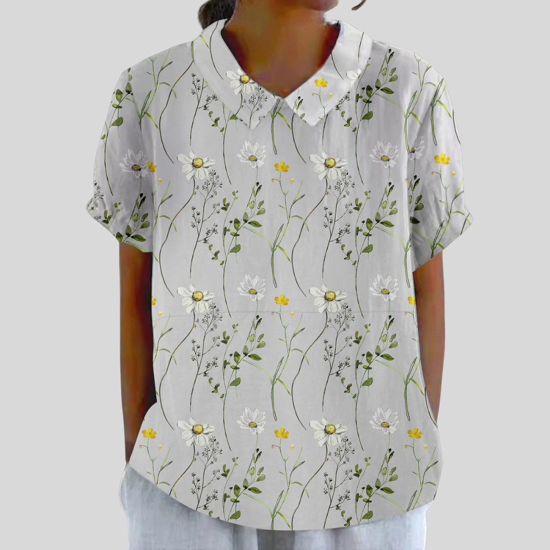 A woman wearing a flowing floral top with a polo collar, looking feminine and relaxed.