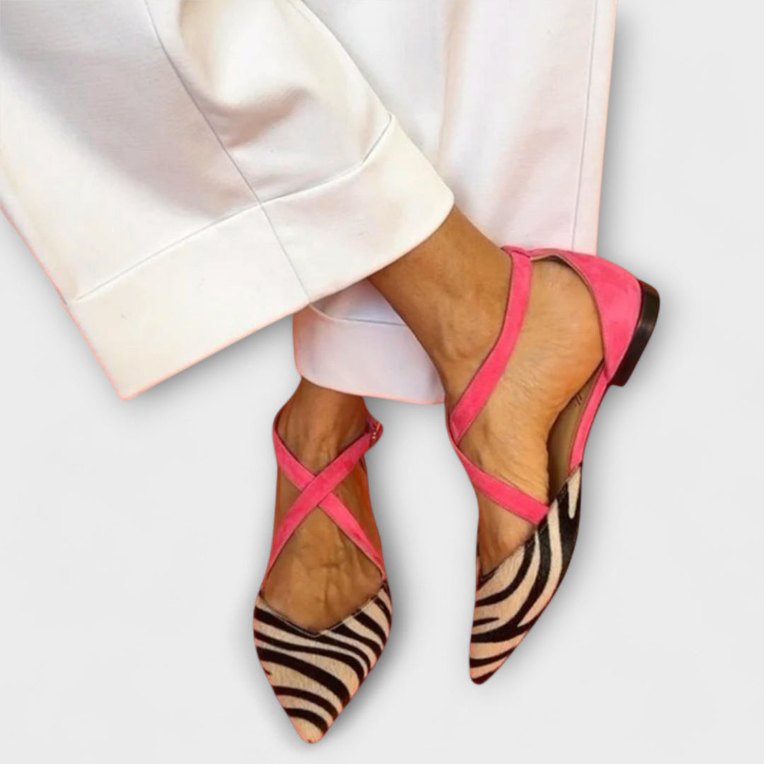 A woman wearing pointed flats with a zebra-print toe and pink cross-over ankle straps.