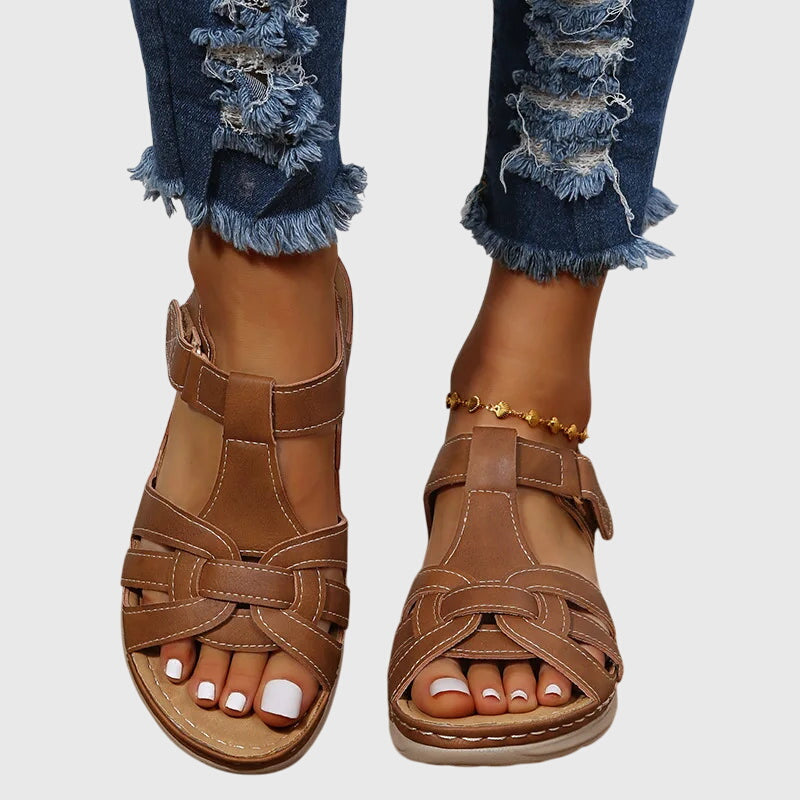 A woman wearing brown woven-effect strap sandals with a cushioned insole and adjustable strap.
