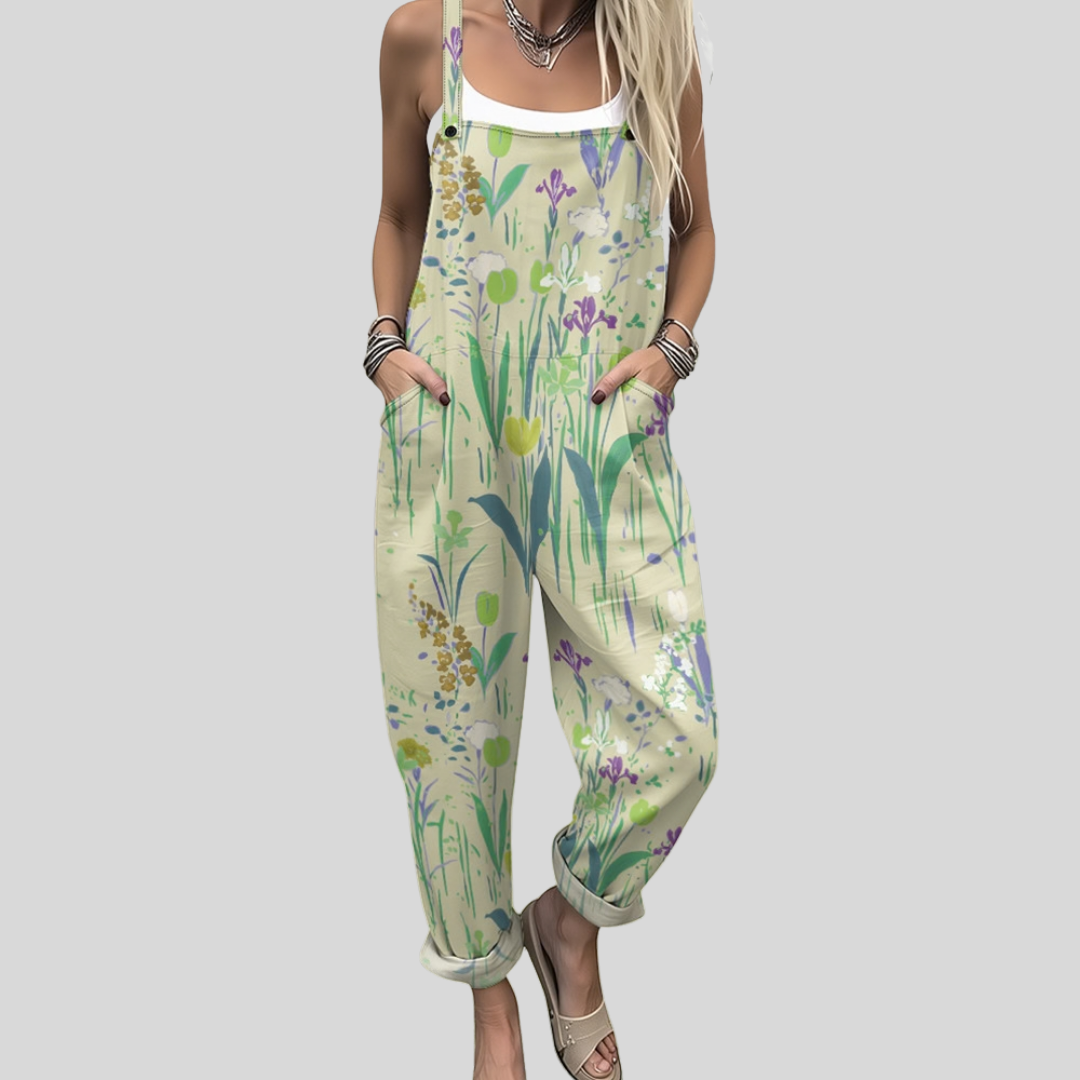 A woman wearing pale overalls printed with green and lilac watercolour meadow flowers, relaxed outdoors.