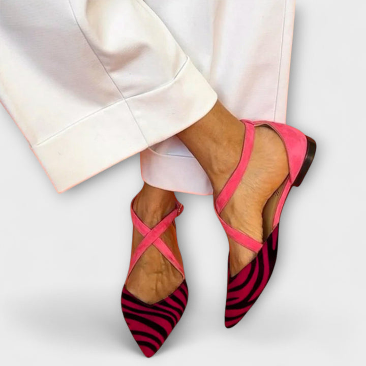 A woman wearing pointed flats with a zebra-print toe and pink cross-over ankle straps.
