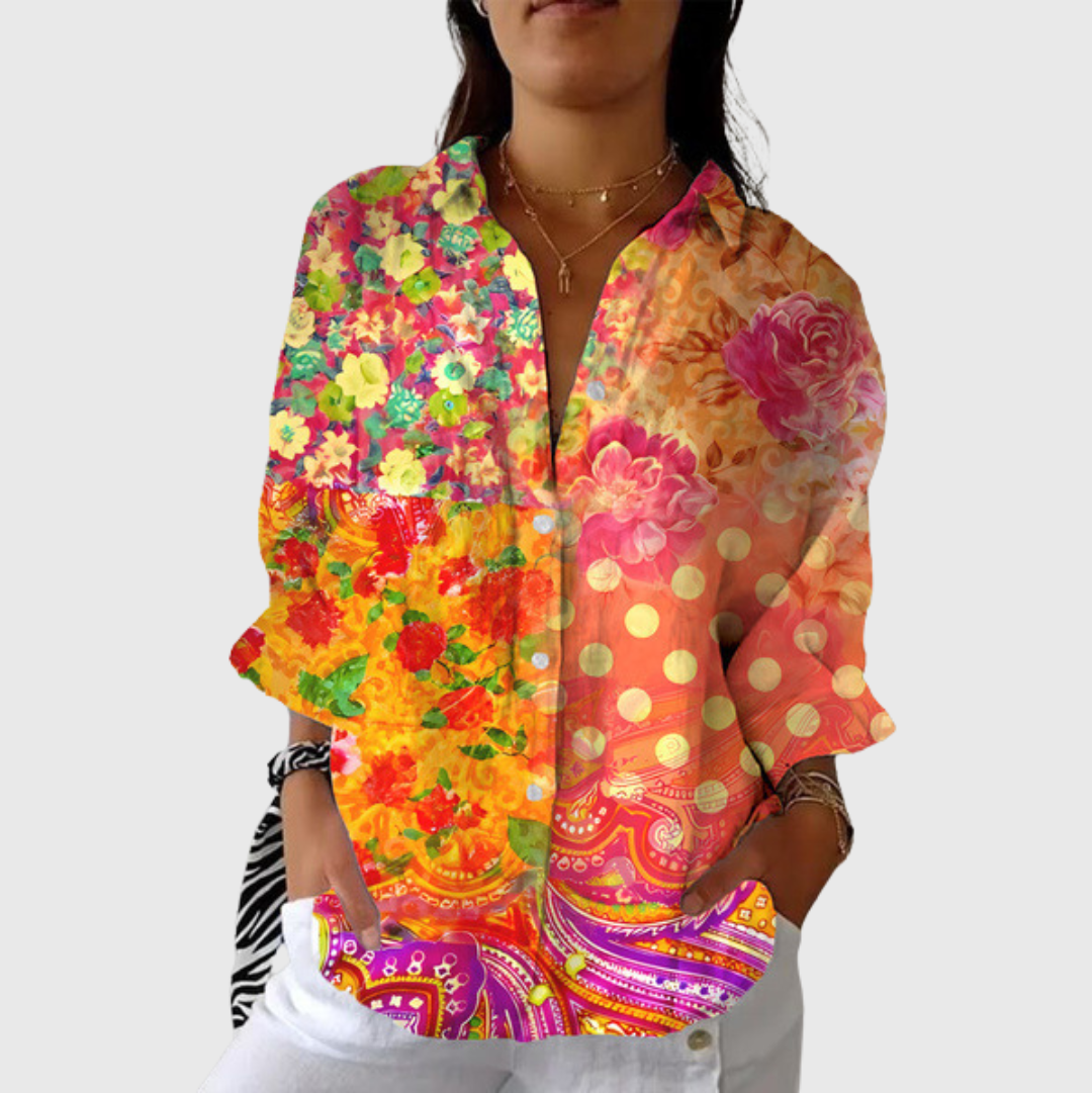A woman wearing a flowing floral printed blouse with pants, smiling outdoors