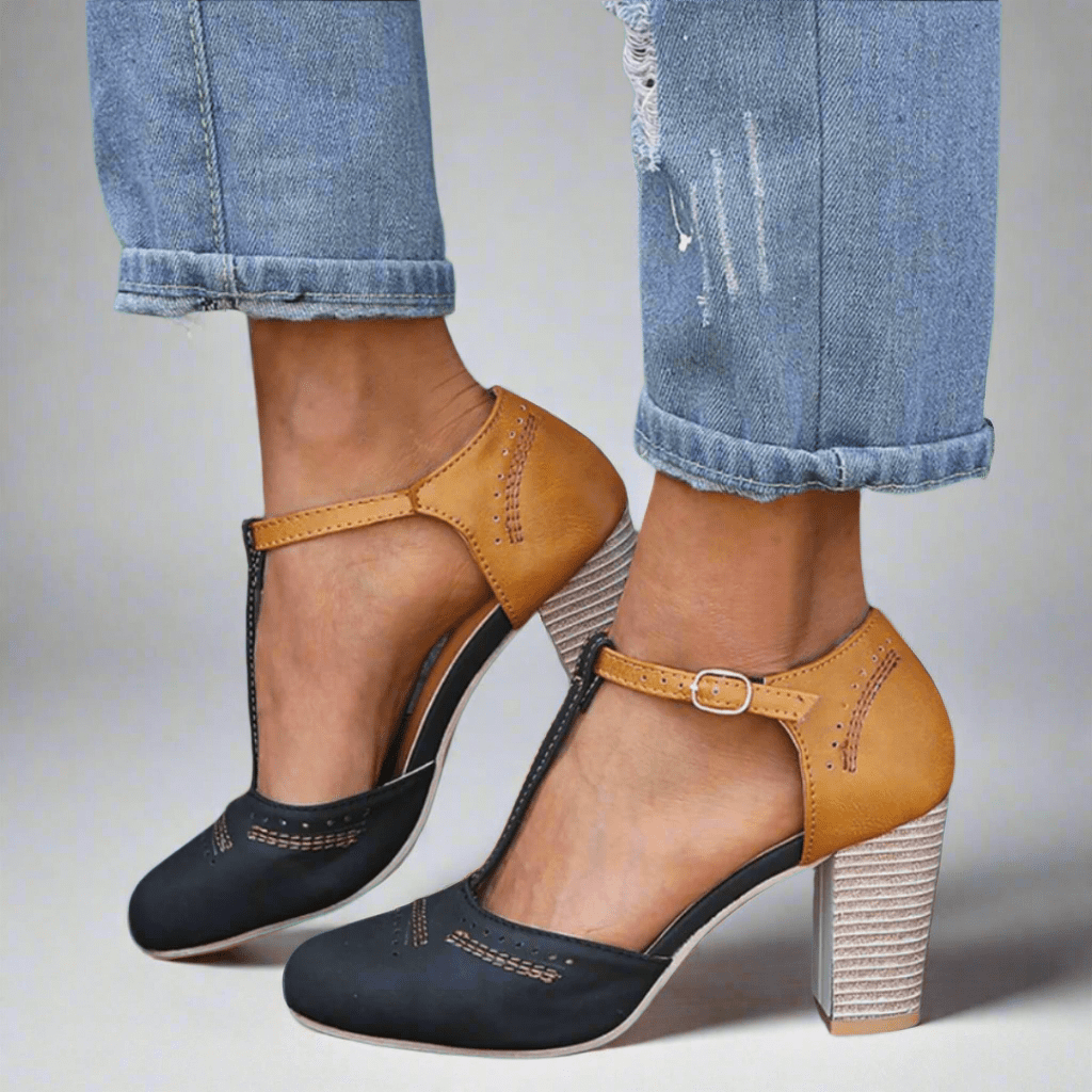 A woman wearing two-tone T-strap heels in navy and mustard tan with a stacked block heel, styled with cropped jeans.