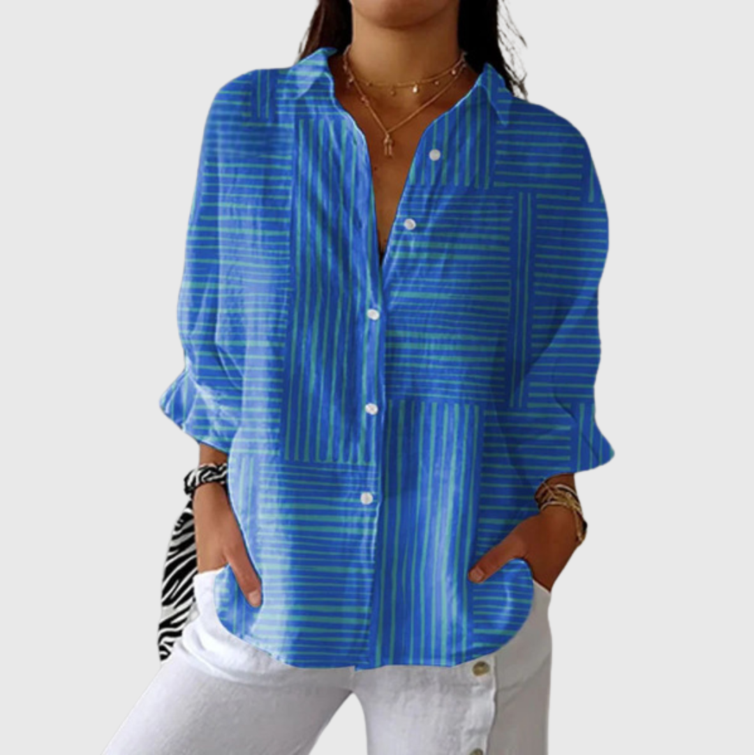 A woman wearing a loose blue striped blouse with white pants, relaxed and smiling