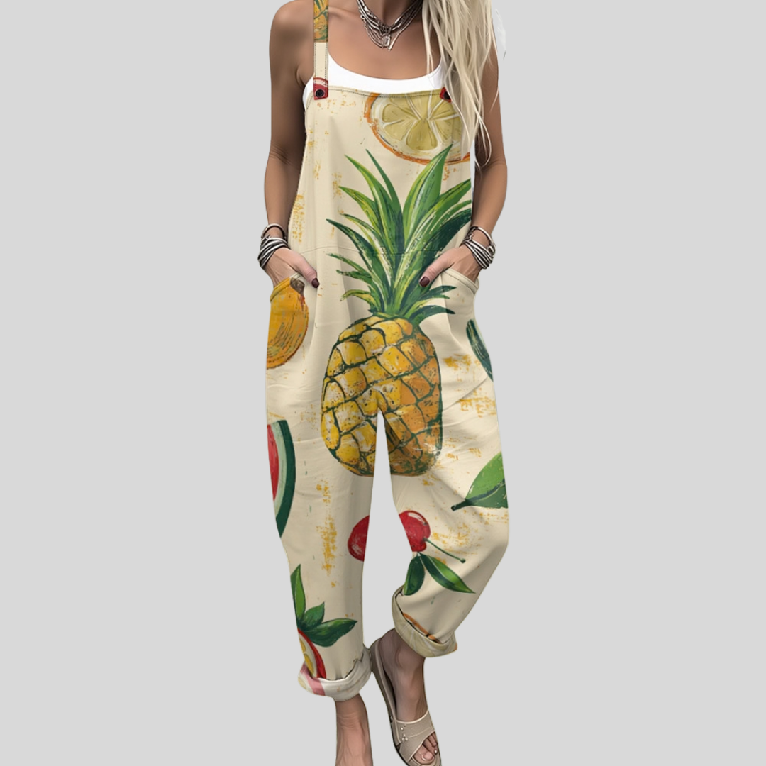 A woman wearing cream overalls printed with pineapples, watermelon and lemons, with adjustable straps.