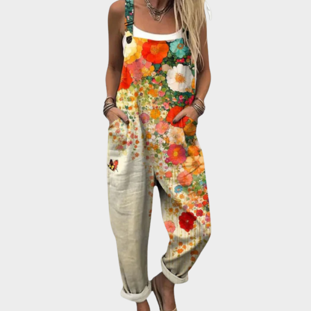 A woman wearing cream overalls with a bright floral print of poppies and daisies, with adjustable straps.