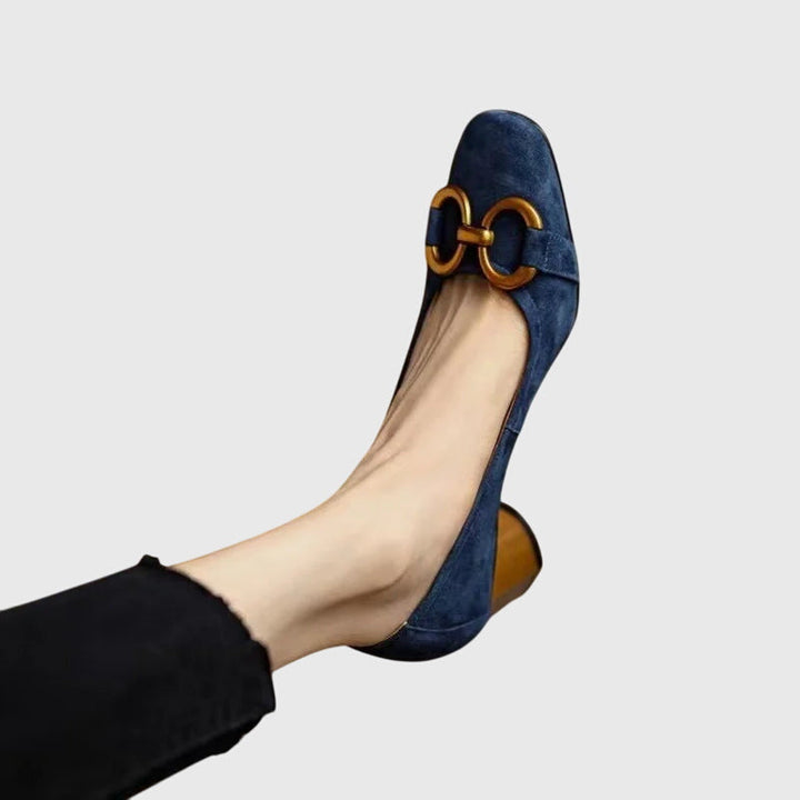 A woman wearing khaki block-heel court shoes with a gold buckle detail, standing with ease and confidence.