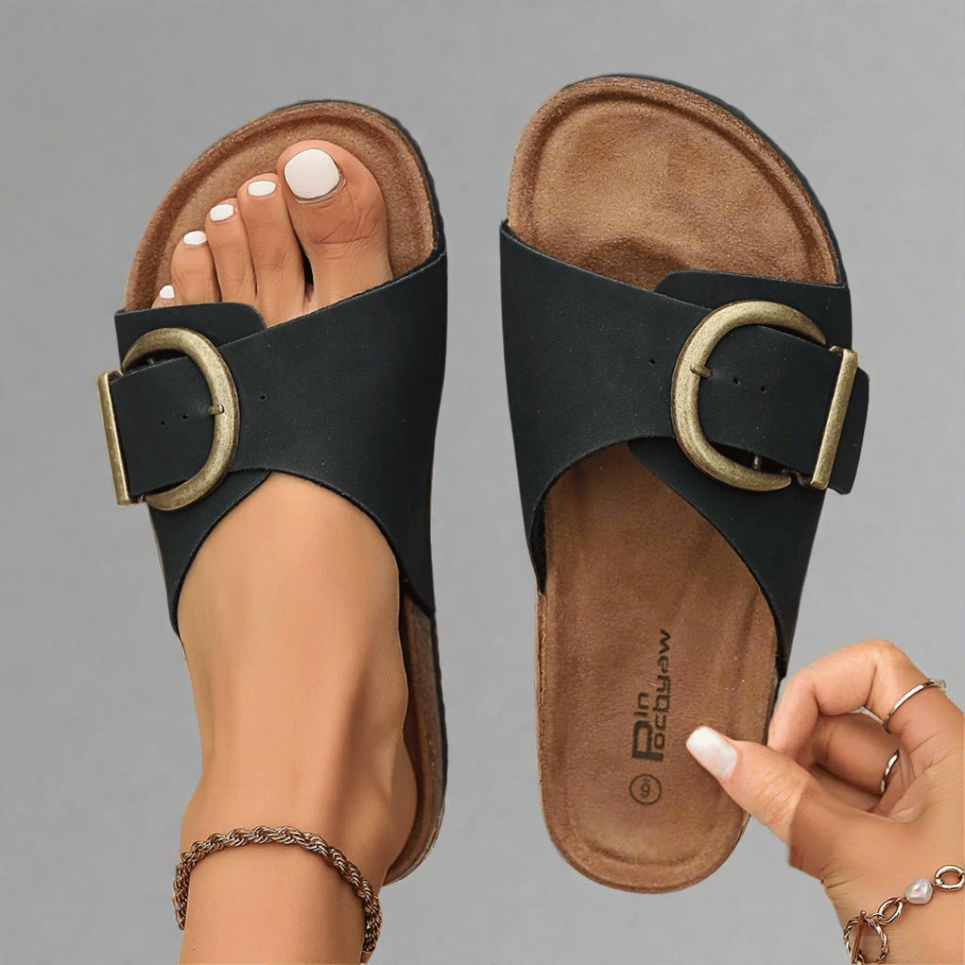 A woman wearing minimalist buckle slip-on sandals with a wide crossover strap on a summer evening.