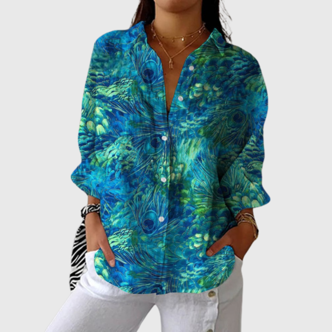 A woman in a teal peacock-feather print button-front blouse worn loosely over jeans