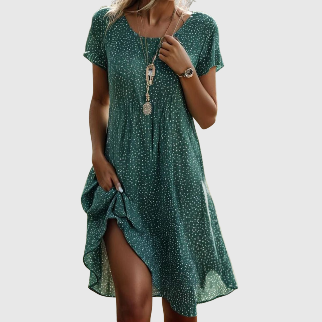 Woman wearing the Cynthia speckled summer dress in green, smiling in the sunshine outdoors.