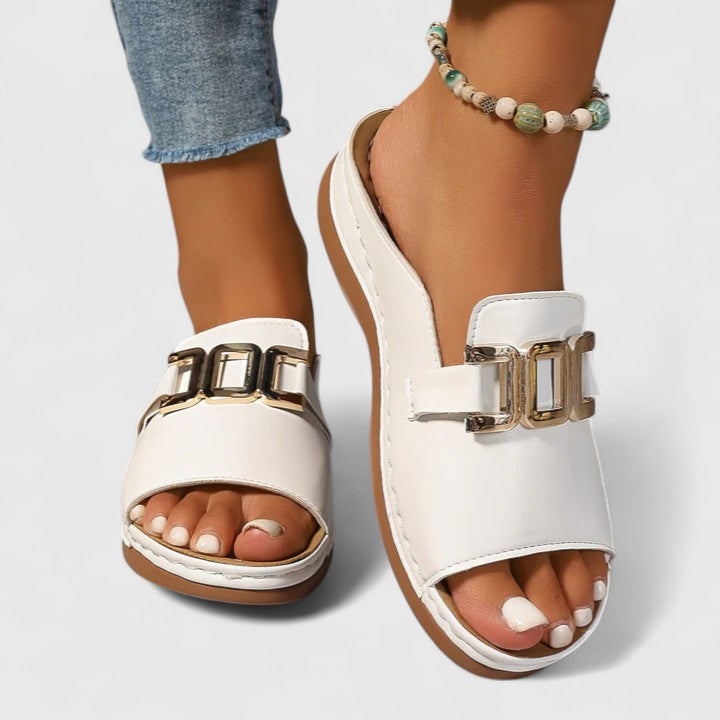 A woman wearing white comfort slides with a golden front trim and a cushioned sole.