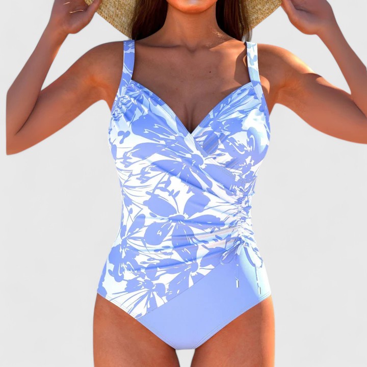 A woman by the water in an elegant printed swimsuit, poised and confident in the summer sun.