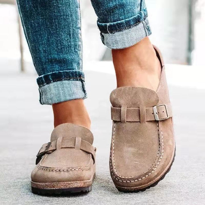 A woman wearing soft taupe buckle clog mules with cropped jeans on a city stroll.