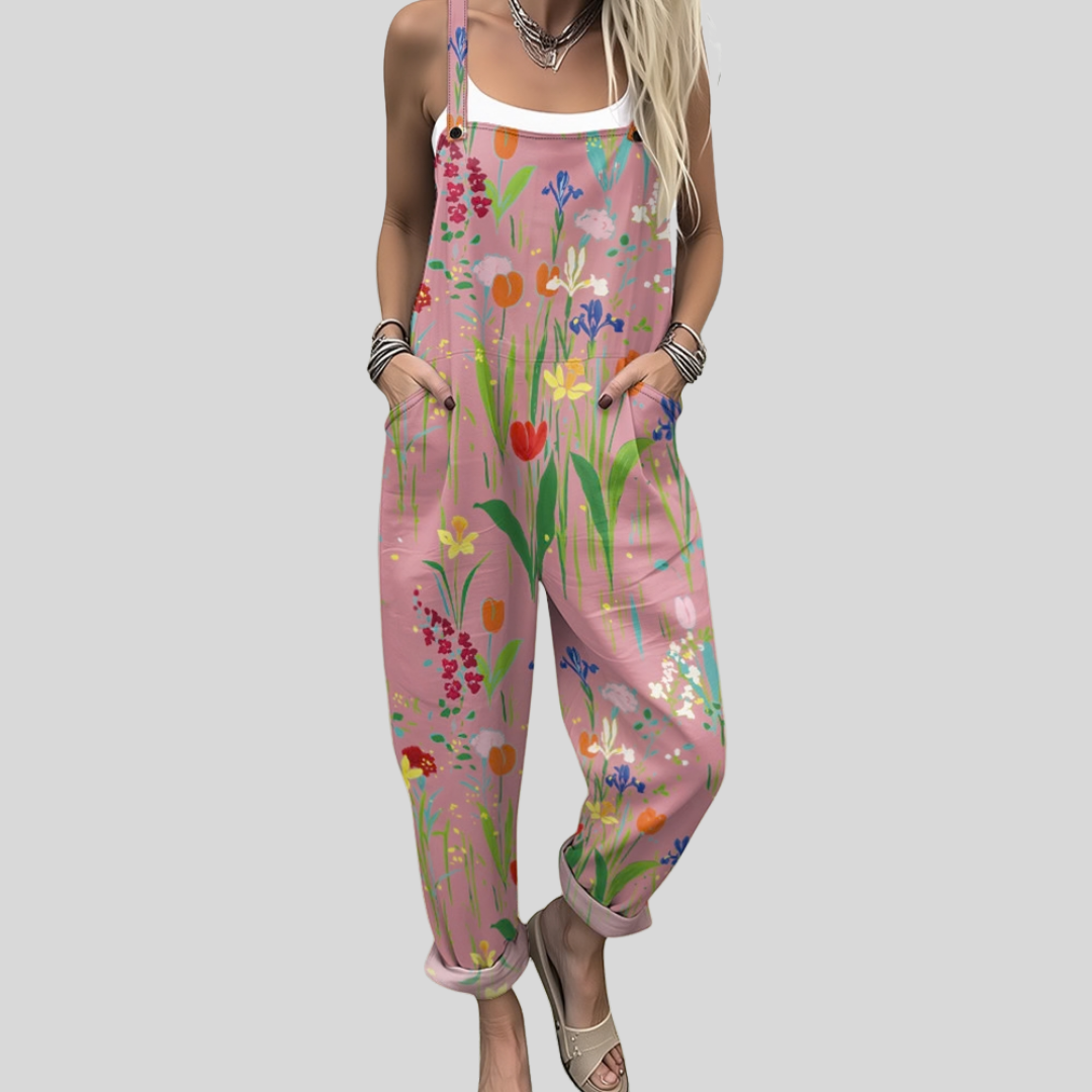 Woman wearing dusty pink overalls printed with dainty colourful wildflowers, standing relaxed outdoors.