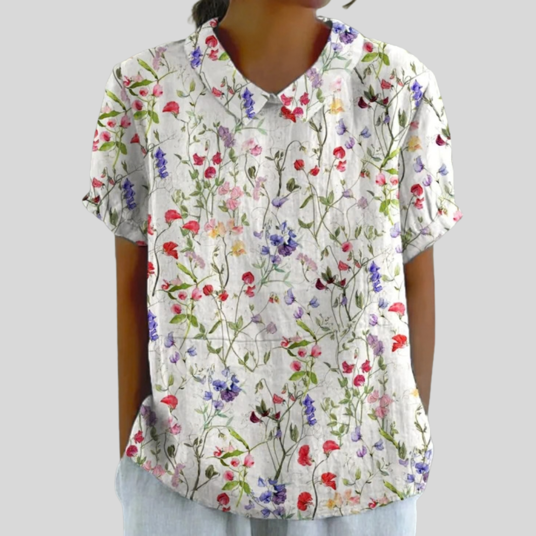 A woman wearing a soft floral top with a structured collar, looking relaxed and elegant.