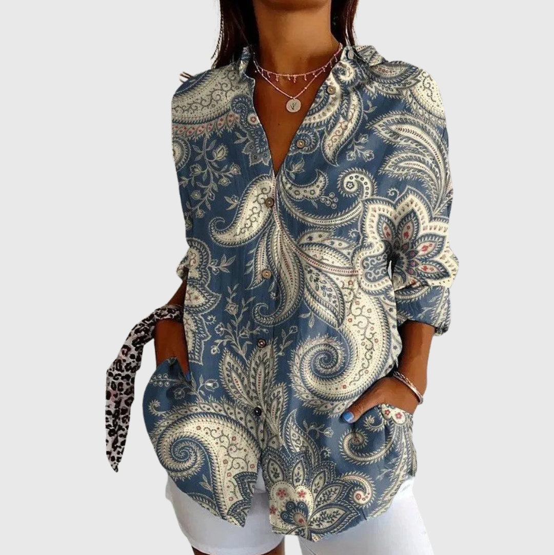 A woman wearing a relaxed colourful printed blouse with adjustable sleeves, styled with pants for an easy day out.