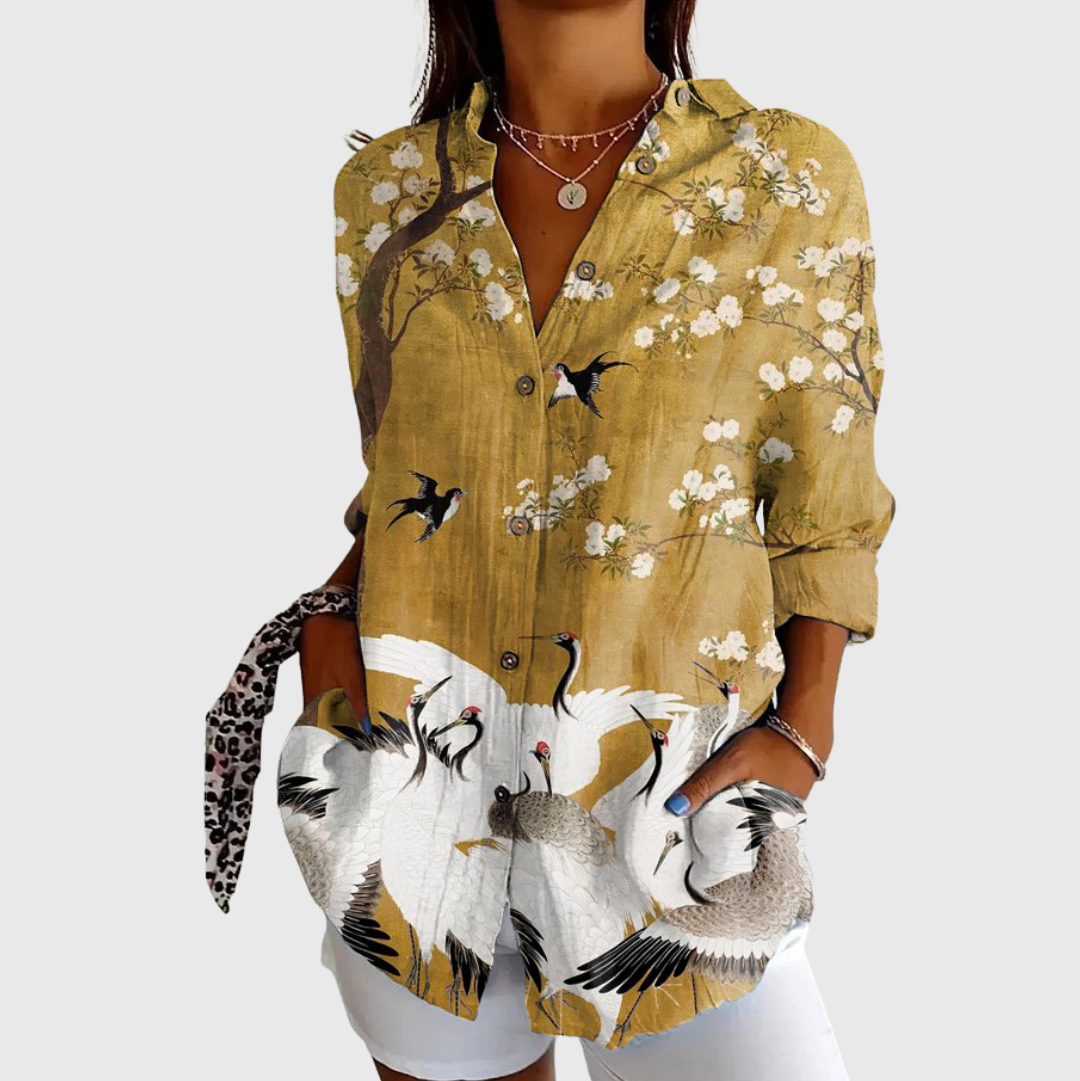 A woman in a golden blouse with a blossom-and-crane print, worn loose