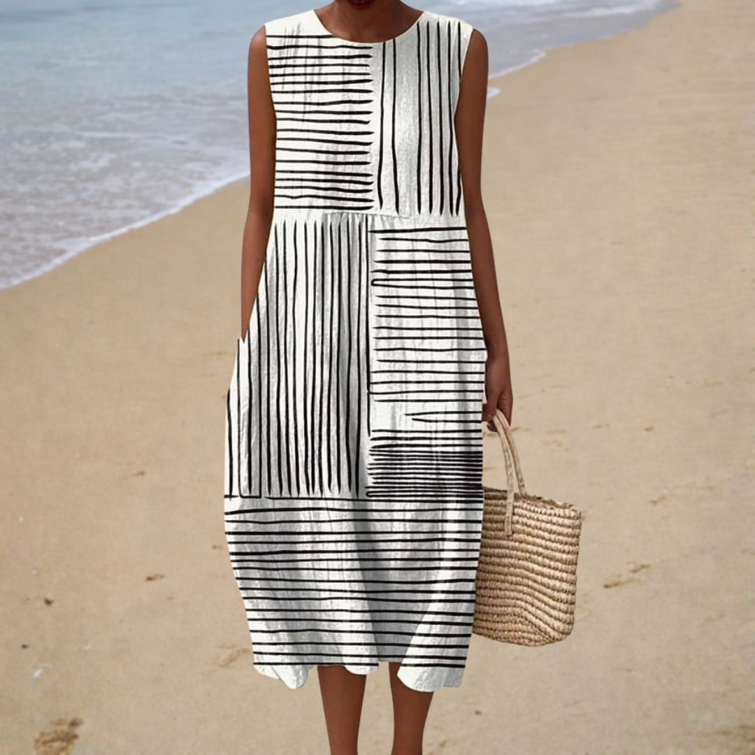 A woman wearing a breezy sleeveless summer dress with an elegant pattern, smiling in the sunshine.