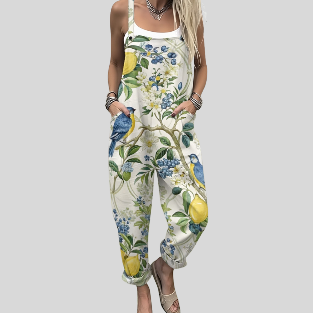 Woman wearing cream overalls printed with lemons, blue berries and a little bird among green branches.