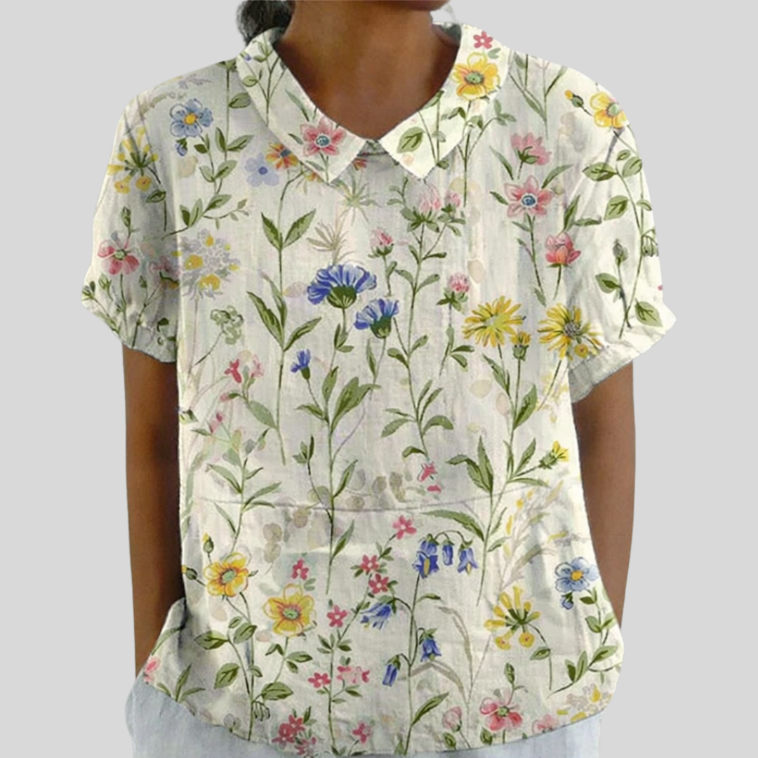 A woman wearing a flowing floral top with a structured polo collar, looking feminine and relaxed.