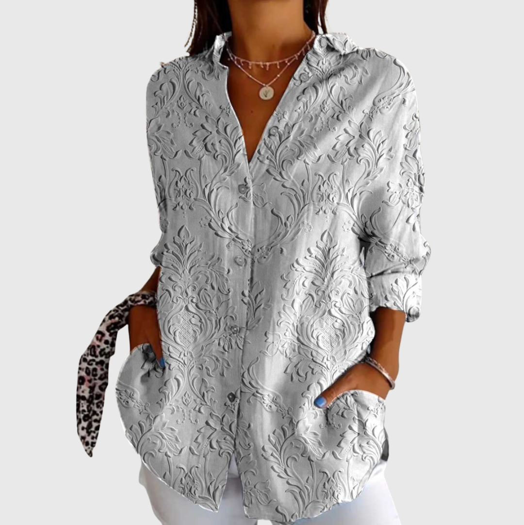 A woman in a soft grey blouse with a subtle tonal damask pattern, worn loosely