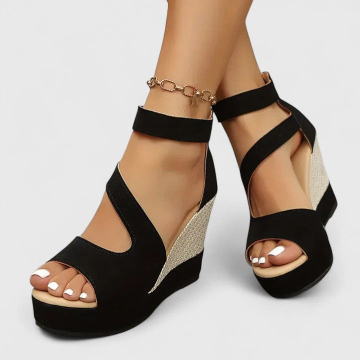 A woman in a summer dress wearing black crossover-strap heeled sandals, standing with easy confidence.
