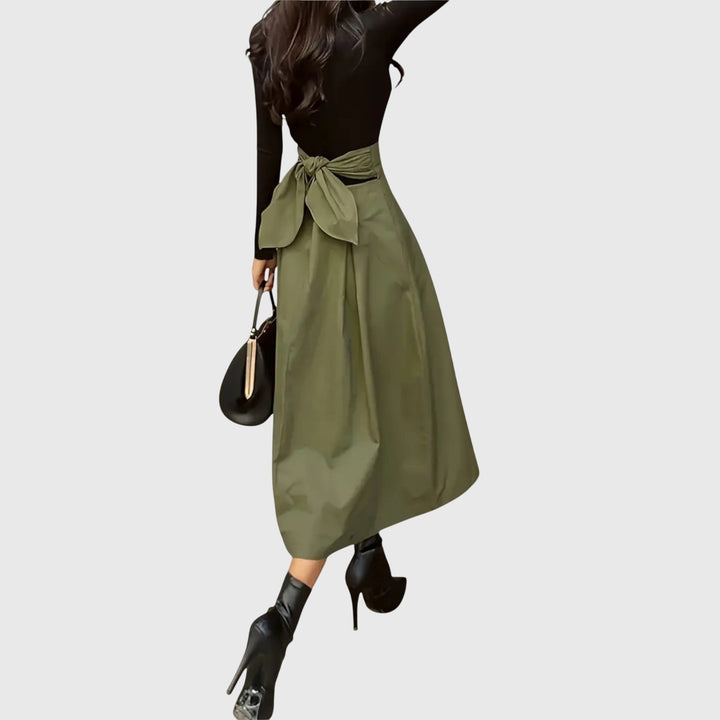 A woman wearing a flared green midi skirt with a belt detail at the waist.