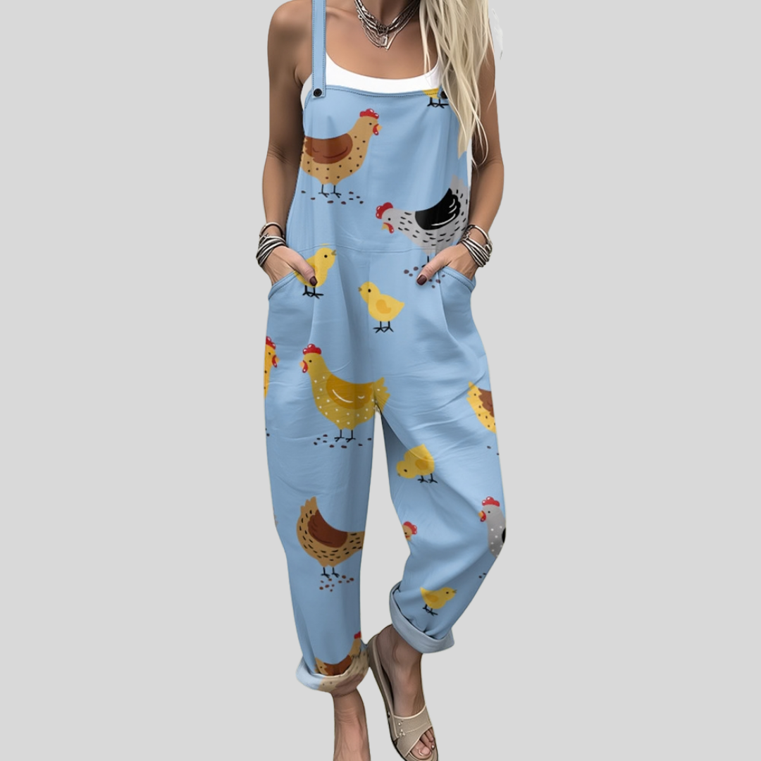 A woman wearing light blue overalls printed with cheerful hens and little chicks, with adjustable straps.