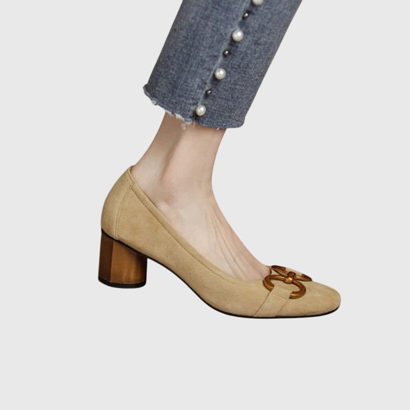 A woman wearing khaki block-heel court shoes with a gold buckle detail, standing with ease and confidence.