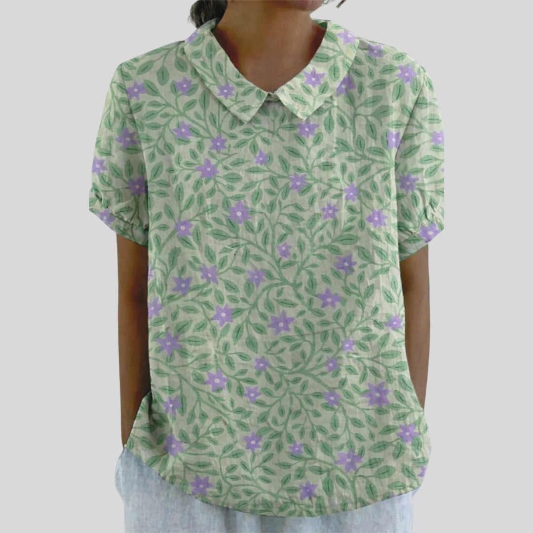A woman wearing a soft floral top with a structured polo collar, looking relaxed and elegant.