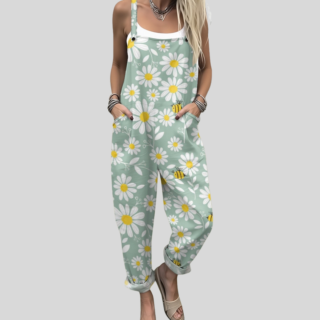 Woman wearing sage green overalls printed with white daisies and little bees, standing in a summer garden.