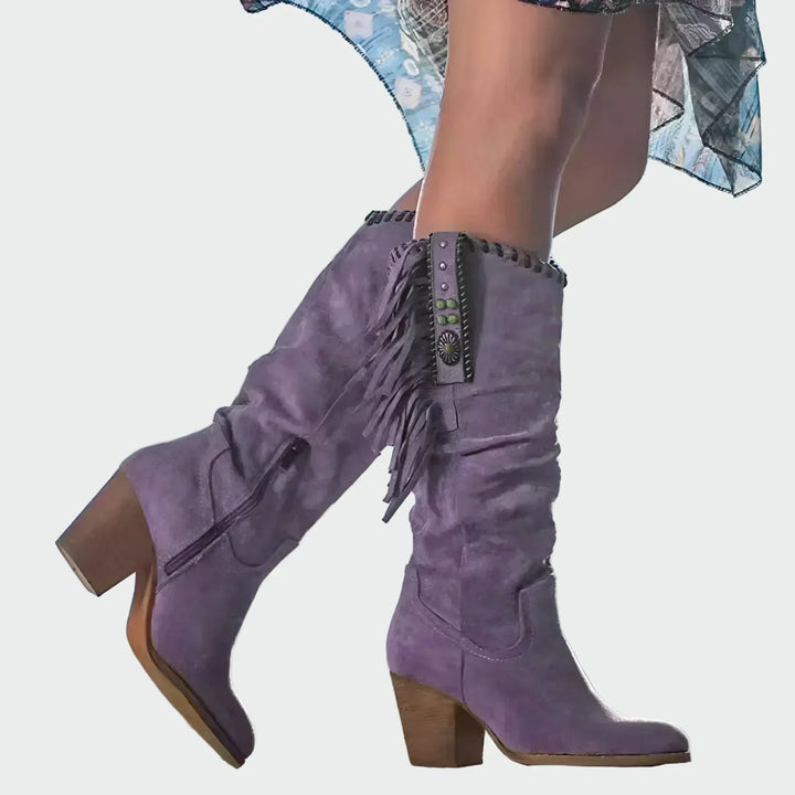 Woman wearing tan fringed boho-Western knee-high boots with a floaty dress at a festival.