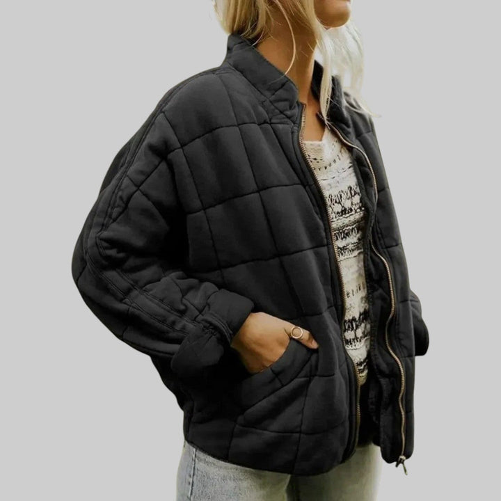 A woman wearing an oversized blush pink quilted jacket with a stand collar and zip front, hand in the pocket.