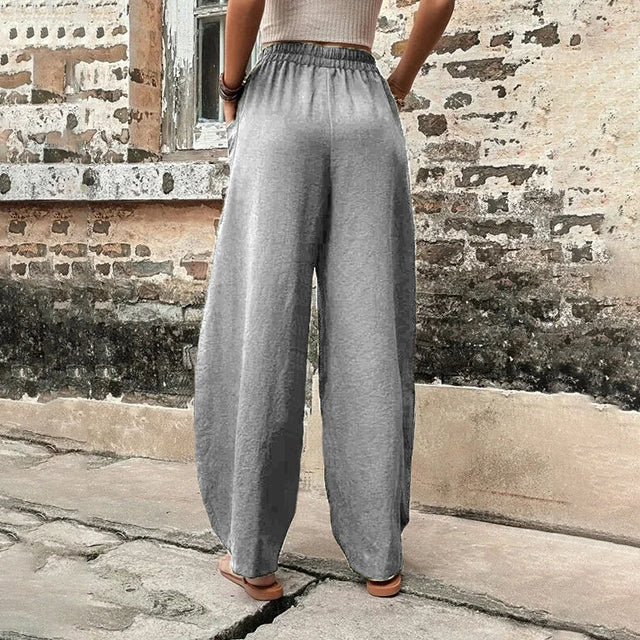 A woman walking in flowing wide-leg pants with big patch pockets and an elegant, draped silhouette.